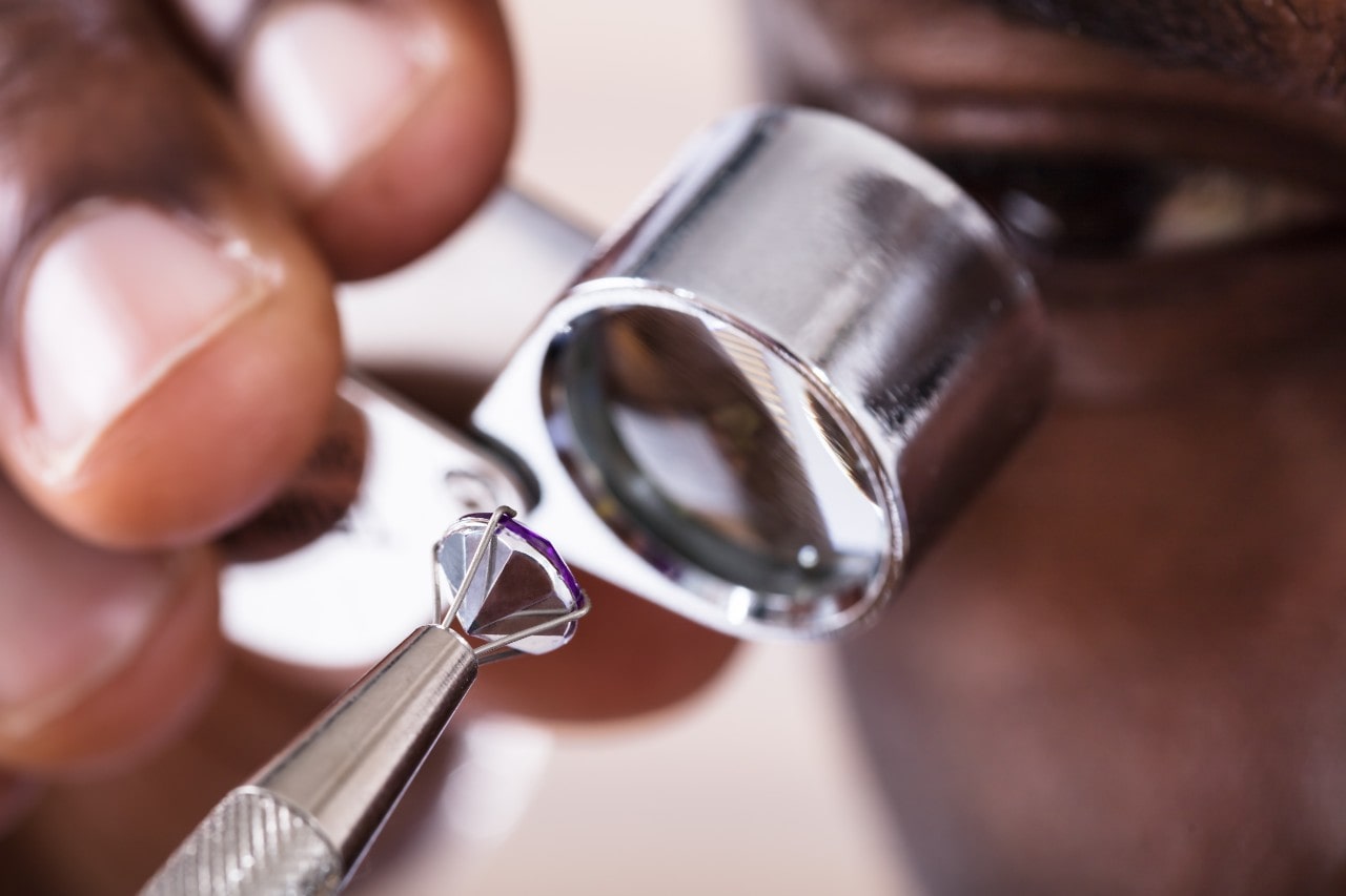 A close-up of a jeweler examines a diamond through a jeweler’s loupe. A close-up of a jeweler examines a diamond through a jeweler’s loupe.