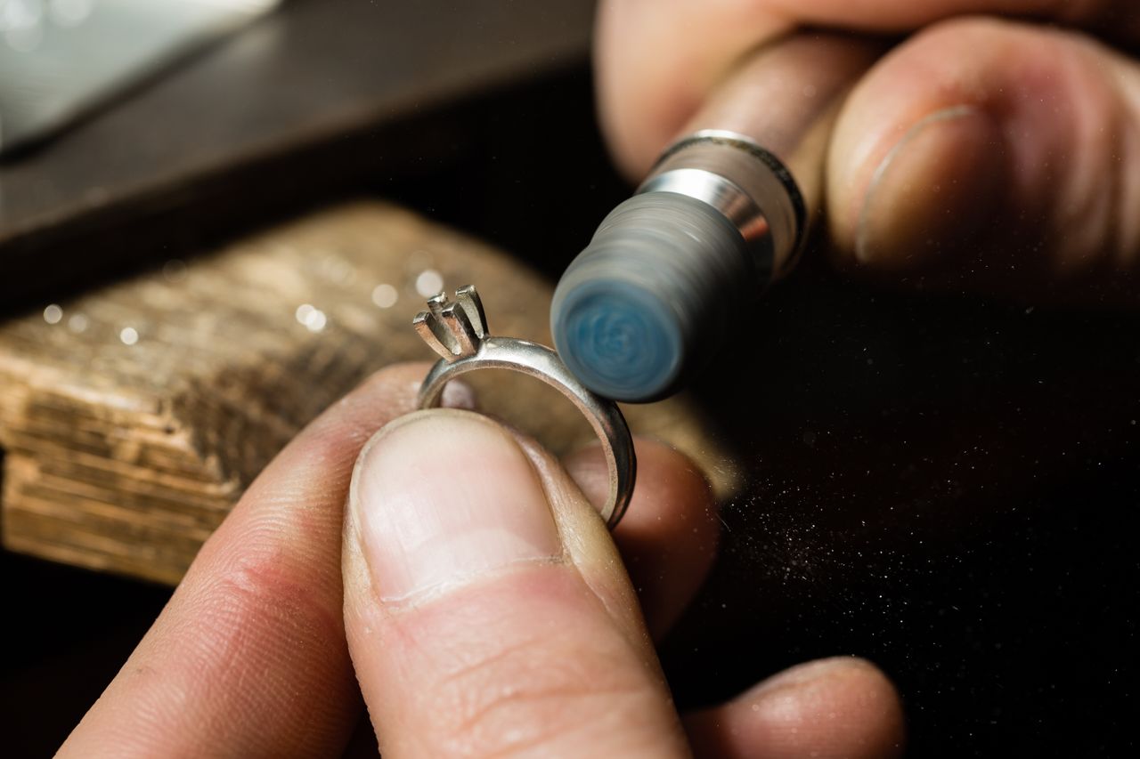 A close-up of a craftsman polishing a solitaire ring setting with a rotary tool. A close-up of a craftsman polishing a solitaire ring setting with a rotary tool.