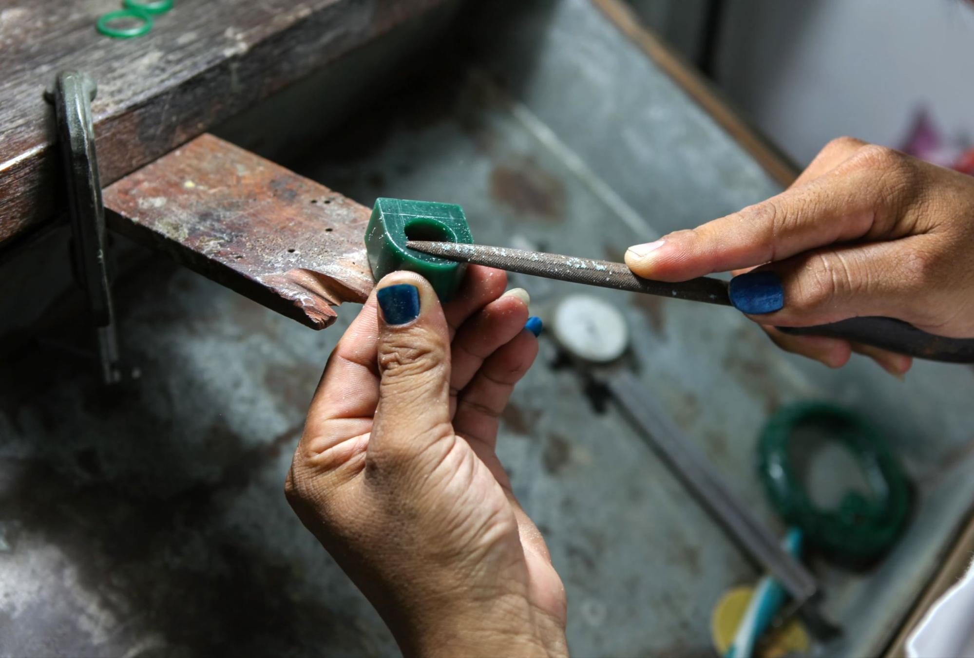 A close-up of a jeweler’s hands carving into a green ring block, creating a custom ring. A close-up of a jeweler’s hands carving into a green ring block, creating a custom ring.