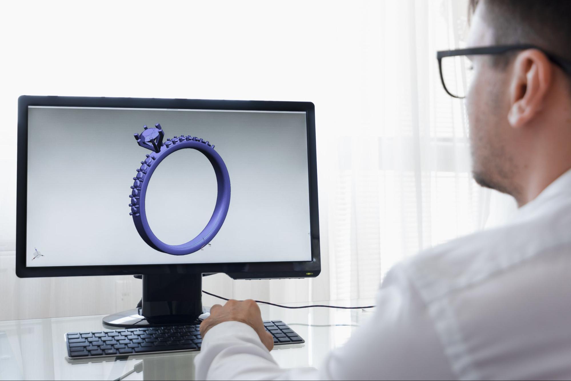 A jeweler looking at a digital rendering of an engagement ring on a computer screen. A jeweler looking at a digital rendering of an engagement ring on a computer screen.