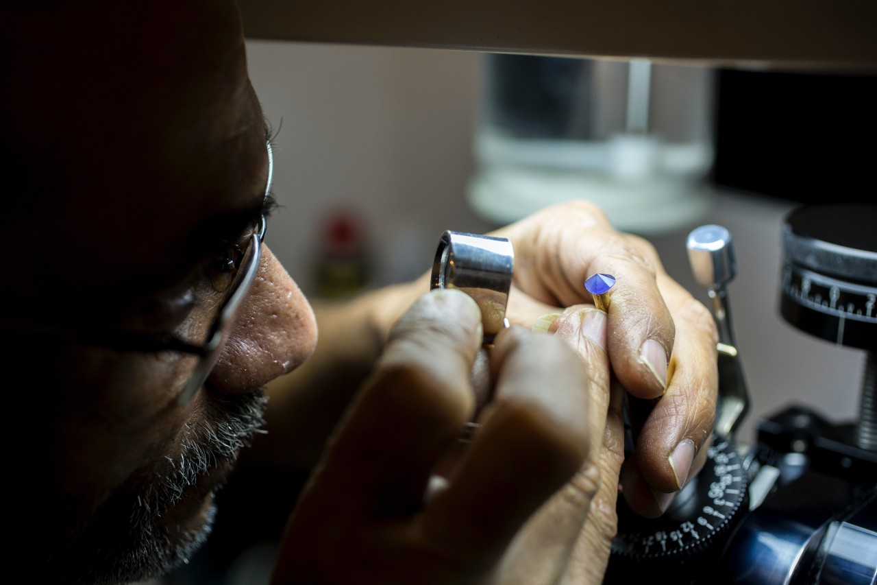 A jeweler examining a gemstone through a small magnifying glass. A jeweler examining a gemstone through a small magnifying glass.