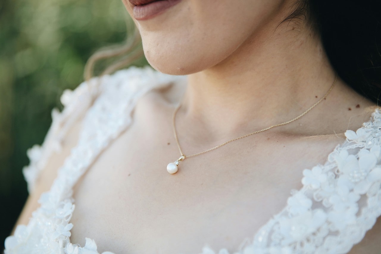 A close-up image of a woman’s neckline adorned with a pearl pendant necklace. A close-up image of a woman’s neckline adorned with a pearl pendant necklace.