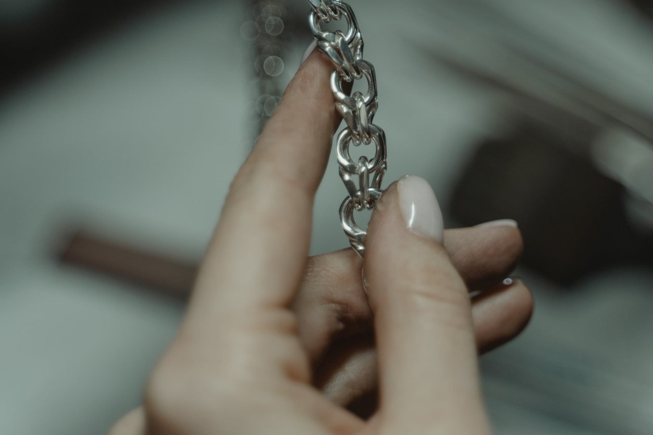 A woman holding a part of a thick silver chain with a blurred, dark background. A woman holding a part of a thick silver chain with a blurred, dark background.
