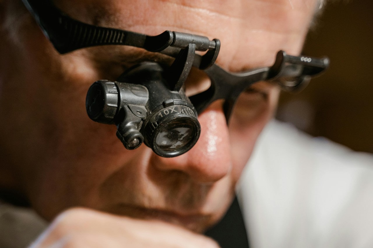A jewelry expert wearing eye gear, closely examining something out of frame. A jewelry expert wearing eye gear, closely examining something out of frame.