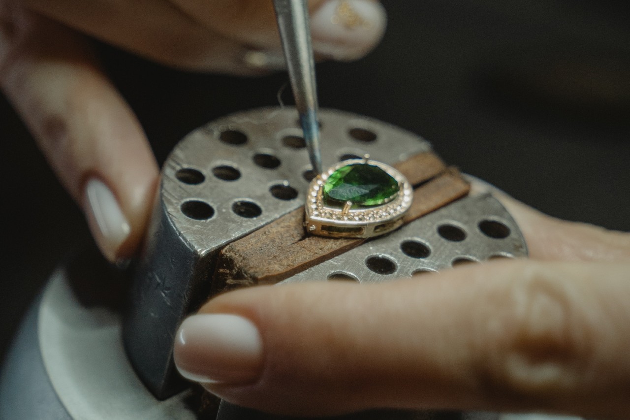 A jewelry professional modifying a pear cut emerald stone with a golden diamond halo. A jewelry professional modifying a pear cut emerald stone with a golden diamond halo.