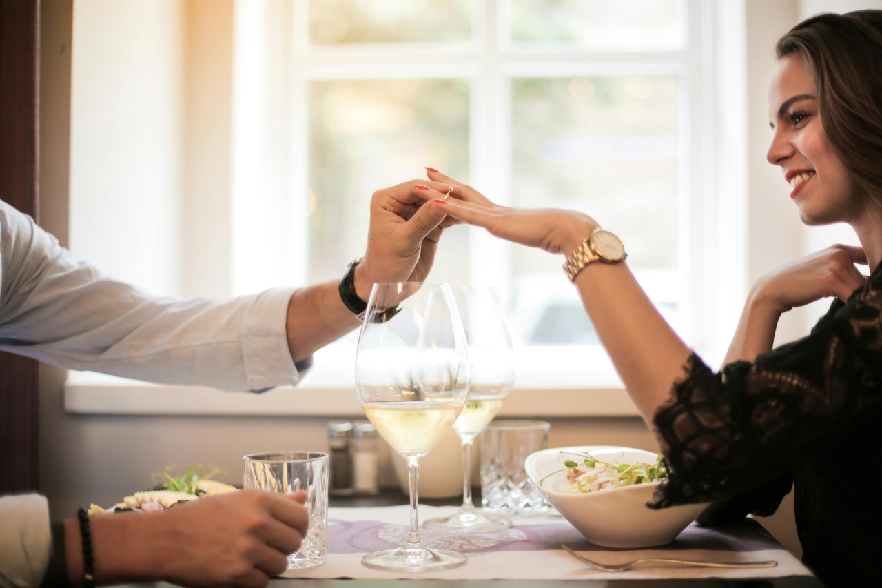 A man putting a diamond ring on a woman’s finger across the dinner table, set with salads and two glasses of white wine. A man putting a diamond ring on a woman’s finger across the dinner table, set with salads and two glasses of white wine.