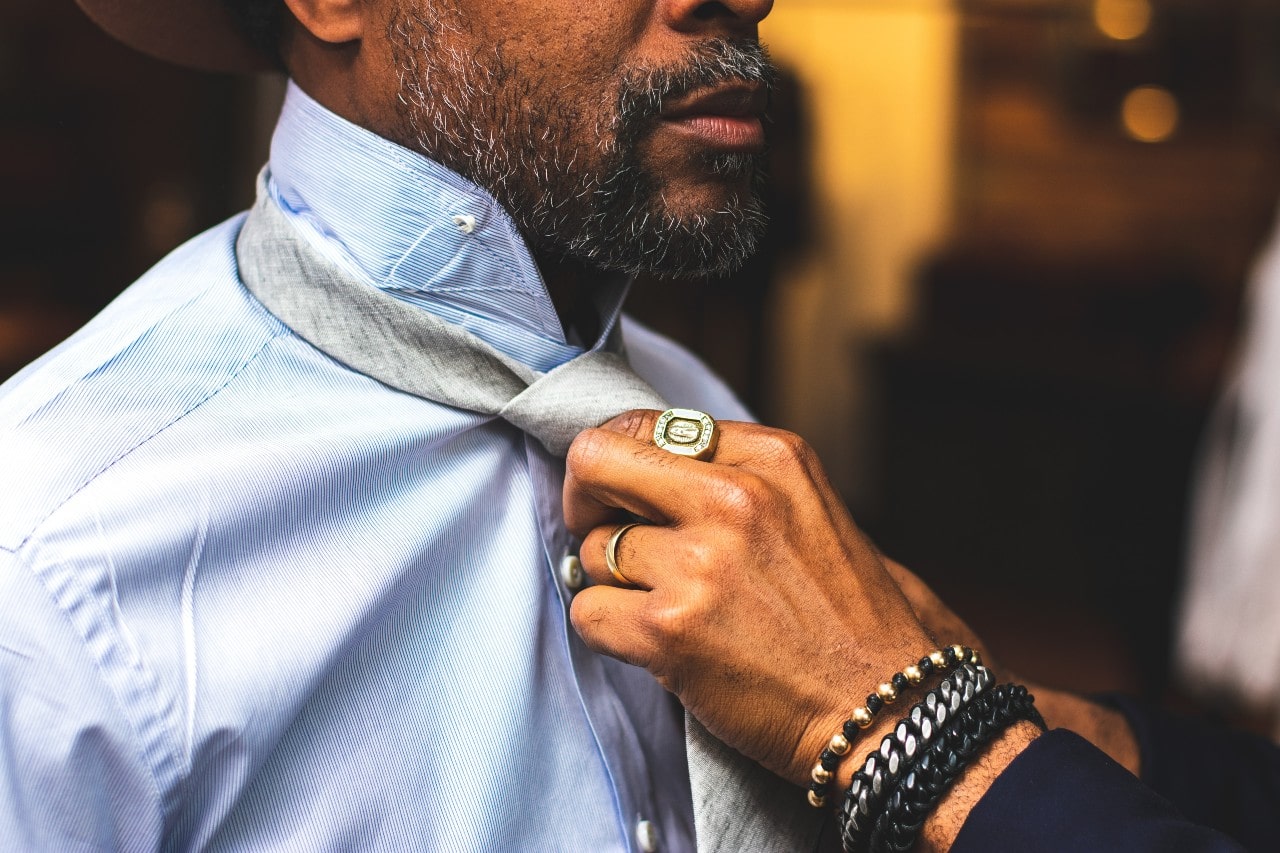 A close-up of a man being dressed by another man wearing a fashionable ring and multiple bracelets. A close-up of a man being dressed by another man wearing a fashionable ring and multiple bracelets.