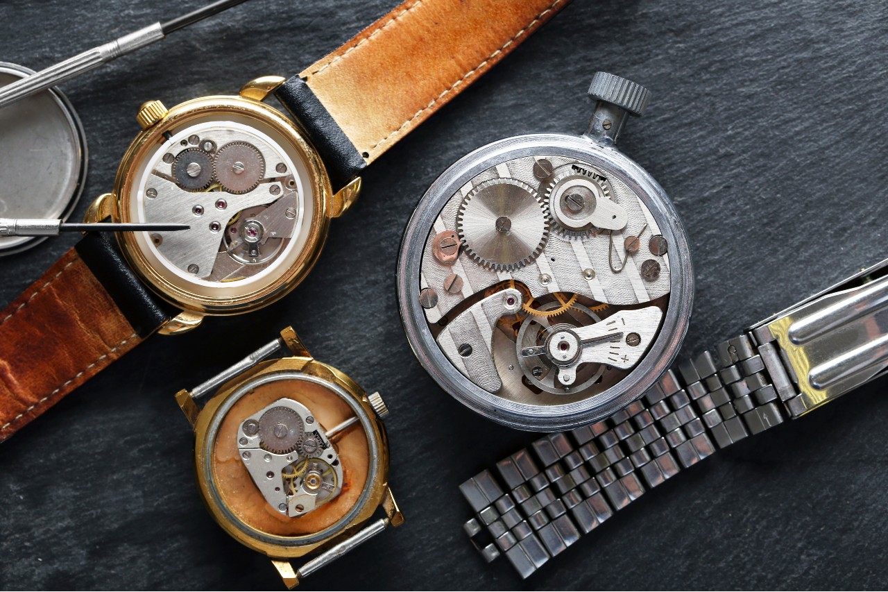 An assortment of vintage wristwatches with their cases open reveals mechanical movements and gears, accompanied by watchmaking tools. An assortment of vintage wristwatches with their cases open reveals mechanical movements and gears, accompanied by watchmaking tools.
