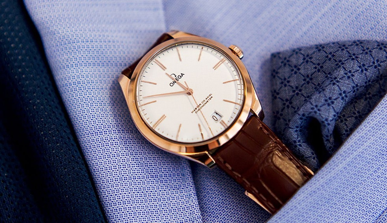 A close-up of a brown leather Omega wristwatch inside a lavender shirt pocket A close-up of a brown leather Omega wristwatch inside a lavender shirt pocket