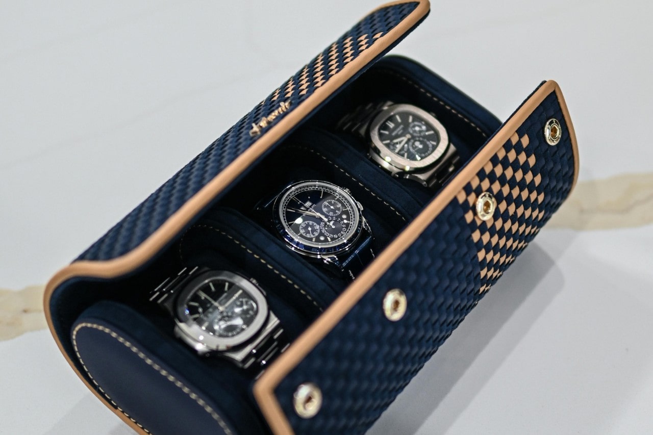 A dark blue watch holder with three metallic watches with black dials inside it. A dark blue watch holder with three metallic watches with black dials inside it.